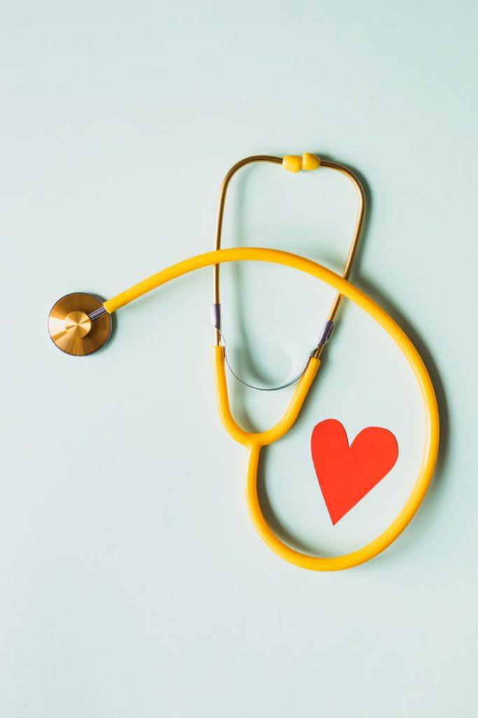 medical stethoscope with red paper heart on blue surface